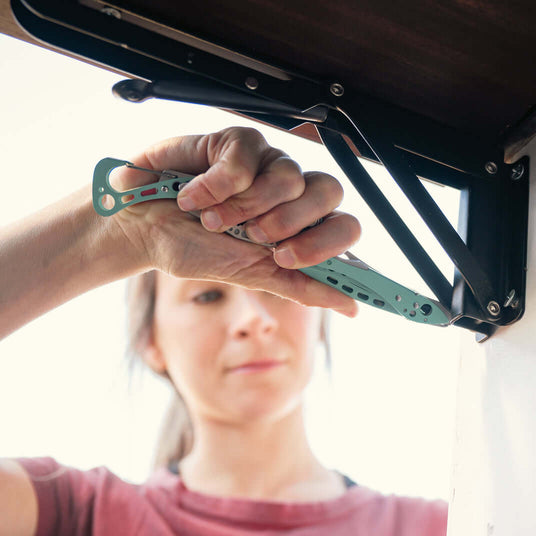Translation missing: fr.Person using a Leatherman Skeletool CX multi-tool to adjust hardware on a lift mechanism, shown in a close-up with focus on the tool in a compact, lightweight design