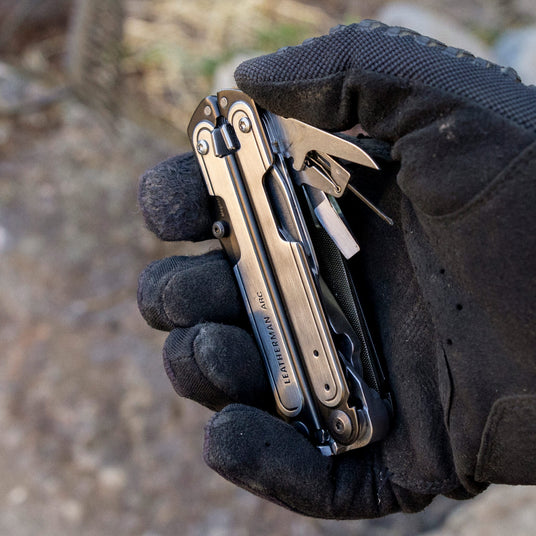 Translation missing: de.Black DLC & Stainless Steel Leatherman ARC® held in a gloved hand, showcasing some tool included tools