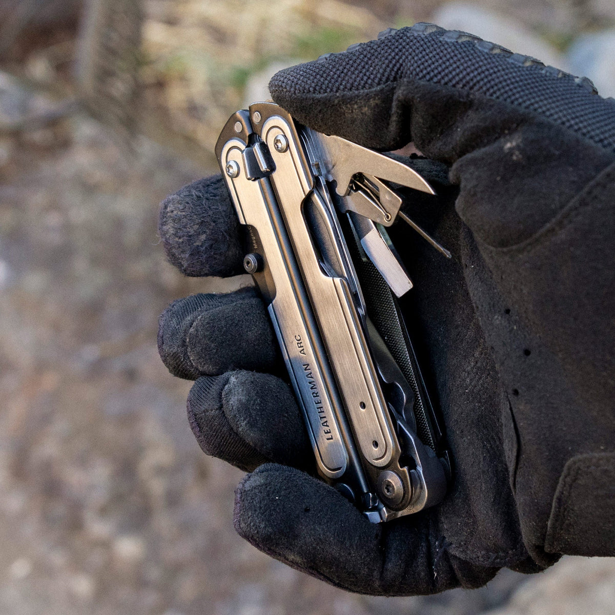 Translation missing: de.Black DLC & Stainless Steel Leatherman ARC® held in a gloved hand, showcasing some tool included tools