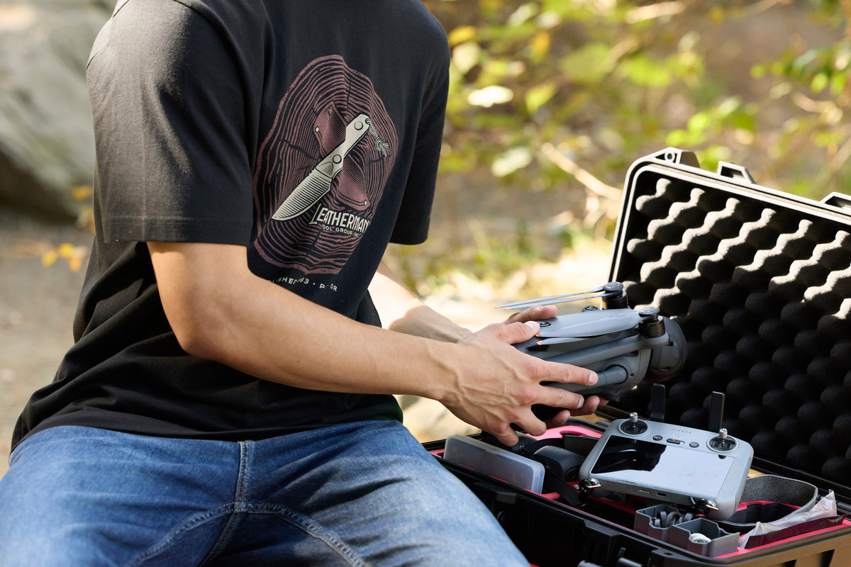 Translation missing: it.A person pulling a drone out of a carrying case while wearing a black Leatherman Blade & Grain Tee with a fixed blade design on the front