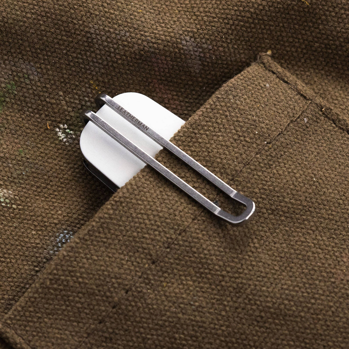 Leatherman Blazer Alpine folding knife clipped inside the pocket of a brown utility garment, with only the white handle and deep-carry pocket clip visible, highlighting convenient everyday carry.