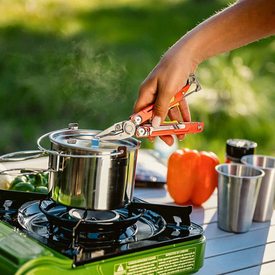 Translation missing: nl.A person cooks on a stove, using Leatherman Signal to handle a pot filled with food