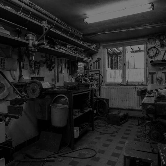 Translation missing: de.Black and white photo of a well-equipped workshop with various tools hanging on the wall, workbenches, and machinery