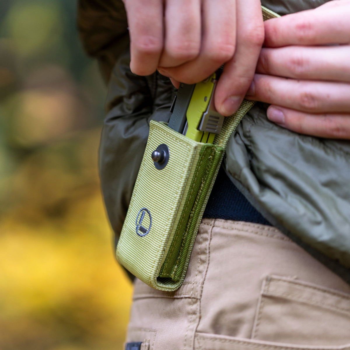 Translation missing: de.Person wearing a green jacket holstering a Mossy Slate Leatherman Rebar® in a matching sheath on their hip