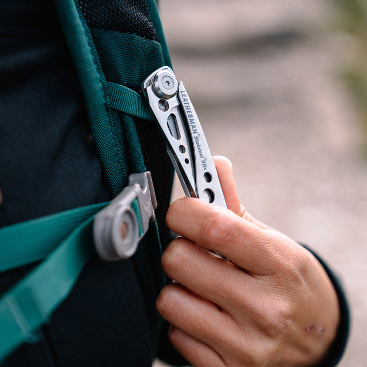 Translation missing: fr.Hand clipping a stainless steel Skeletool KBX pocket knife onto a backpack strap