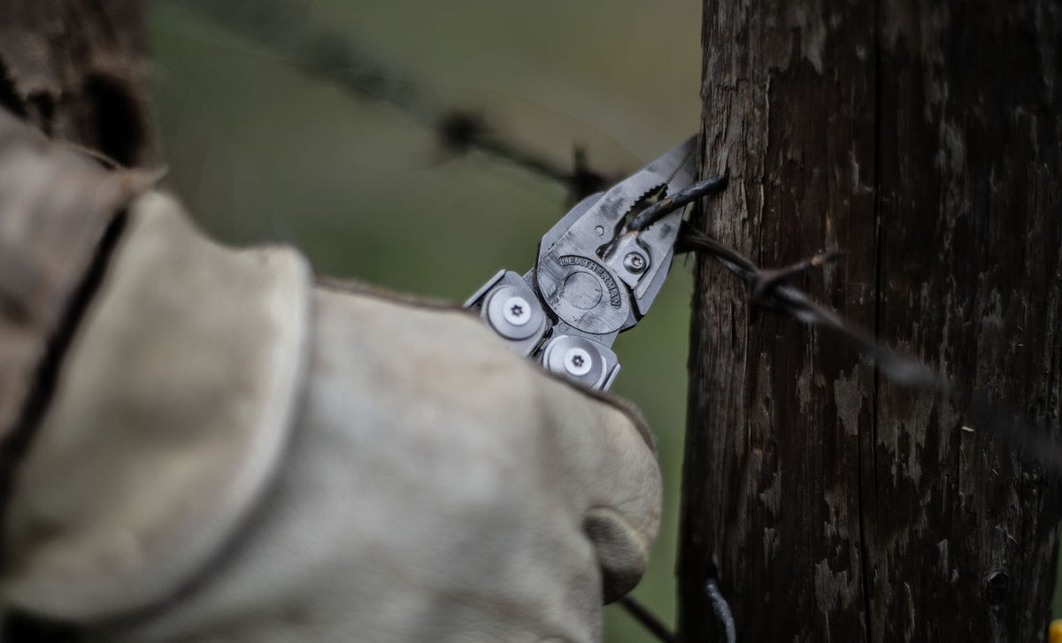 Translation missing: de.Person using a stainless steel Leatherman Surge® multitool pliers on barbed wire attached to a wooden post