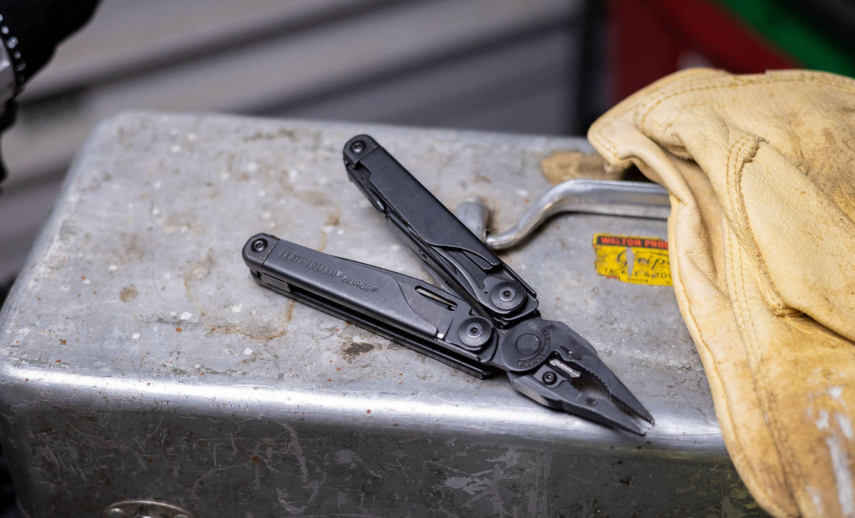 Translation missing: de.Black Leatherman Surge® multi-tool resting on a metal toolbox beside gloves