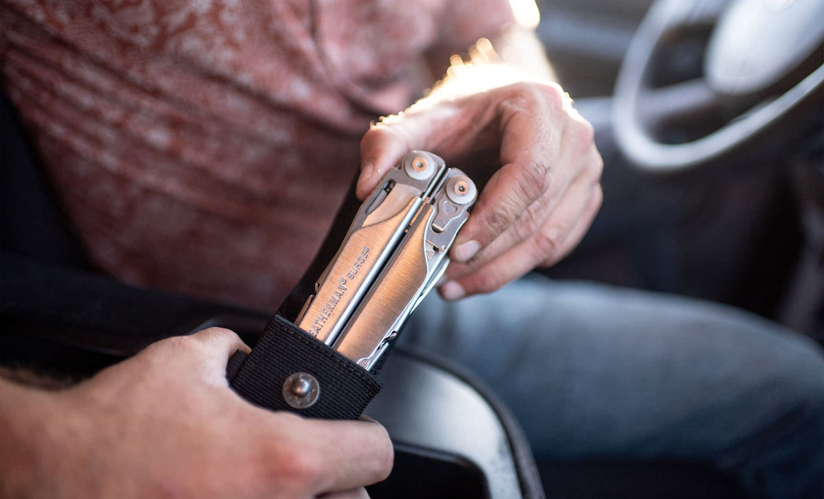 Translation missing: de.Person pulling a stainless steel Leatherman Surge® multitool from its sheath while sitting in a car