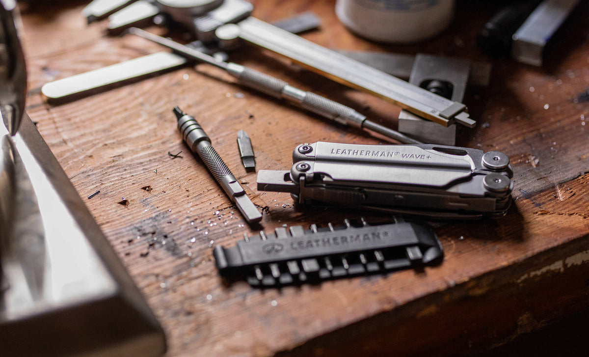 Translation missing: de.Stainless Steel Leatherman Wave® Plus multi-tool on a workbench alongside a Leatherman bit kit, bit and bit driver extender