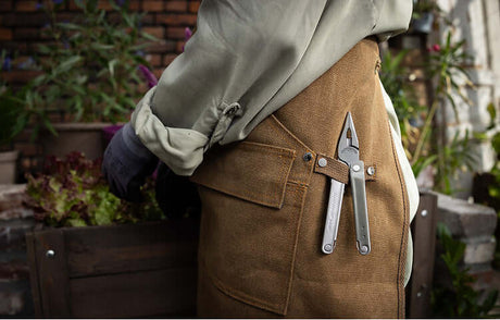 Translation missing: de.A stainless steel Leatherman Bond hanging on the side of a Gardening apron with pliers showing