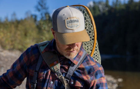Translation missing: de.Man wearing a Leatherman Pacific Northwest Trucker hat walking alongside a stream carrying a backpack and net