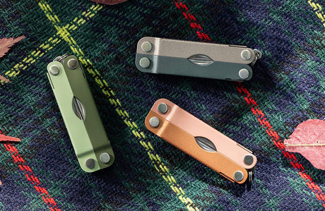 Translation missing: de.Three Micra® multitools in Cardamon, Ginger Peach, and North Star colors displayed on a plaid background with autumn leaves