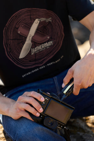 Translation missing: it.A person using a Leatherman Wave Alpha bit driver to tighten a bolt on a camera while wearing a black Blade &amp; Grain Tee
