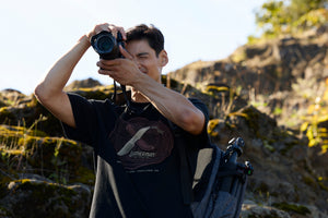 Translation missing: it.A photographer wearing a black Leatherman Blade &amp; Grain Tee while taking a pictures outdoors