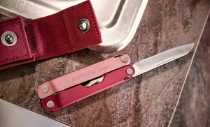 Translation missing: es.Heathered Cranberry Bond open showing knife blade and a Heathered sheath that is open next to a sink on the countertop