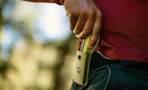 Translation missing: es.Person holding a Mossy Slate Bond half way out of a Moss Sheath that is attached to a belt