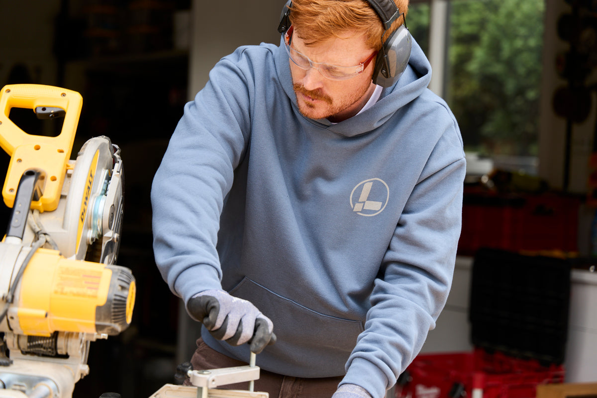 Translation missing: de.A person wearing a storm blue Leatherman Classic Hoodie operating a saw while working on a woodworking project