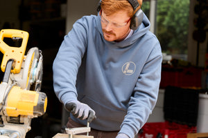 Translation missing: de.A person wearing a storm blue Leatherman Classic Hoodie operating a saw while working on a woodworking project