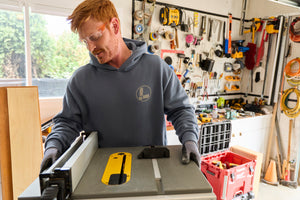 Translation missing: de.A person wearing a storm blue Leatherman Classic Hoodie standing in front of a woodworking tool in a garage workshop