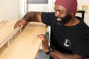 Translation missing: de.A person wearing a black Leatherman Classic Tee using a level tool to level a wooden shelf indoors