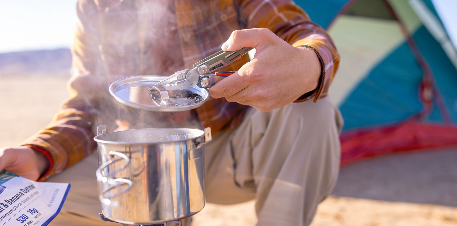 Signal® Tundrascape Limited Edition multitool lifting the lid off a steaming camp pot beside a tent