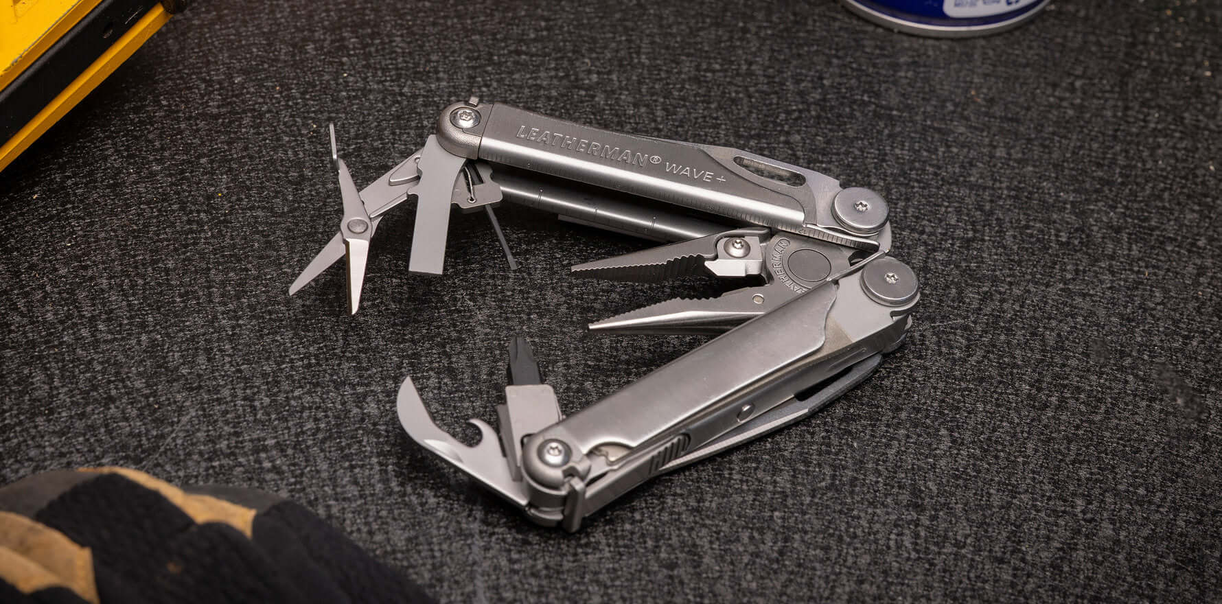 Leatherman Wave Plus multitool with tools fanned on the textured surface of a workbench.