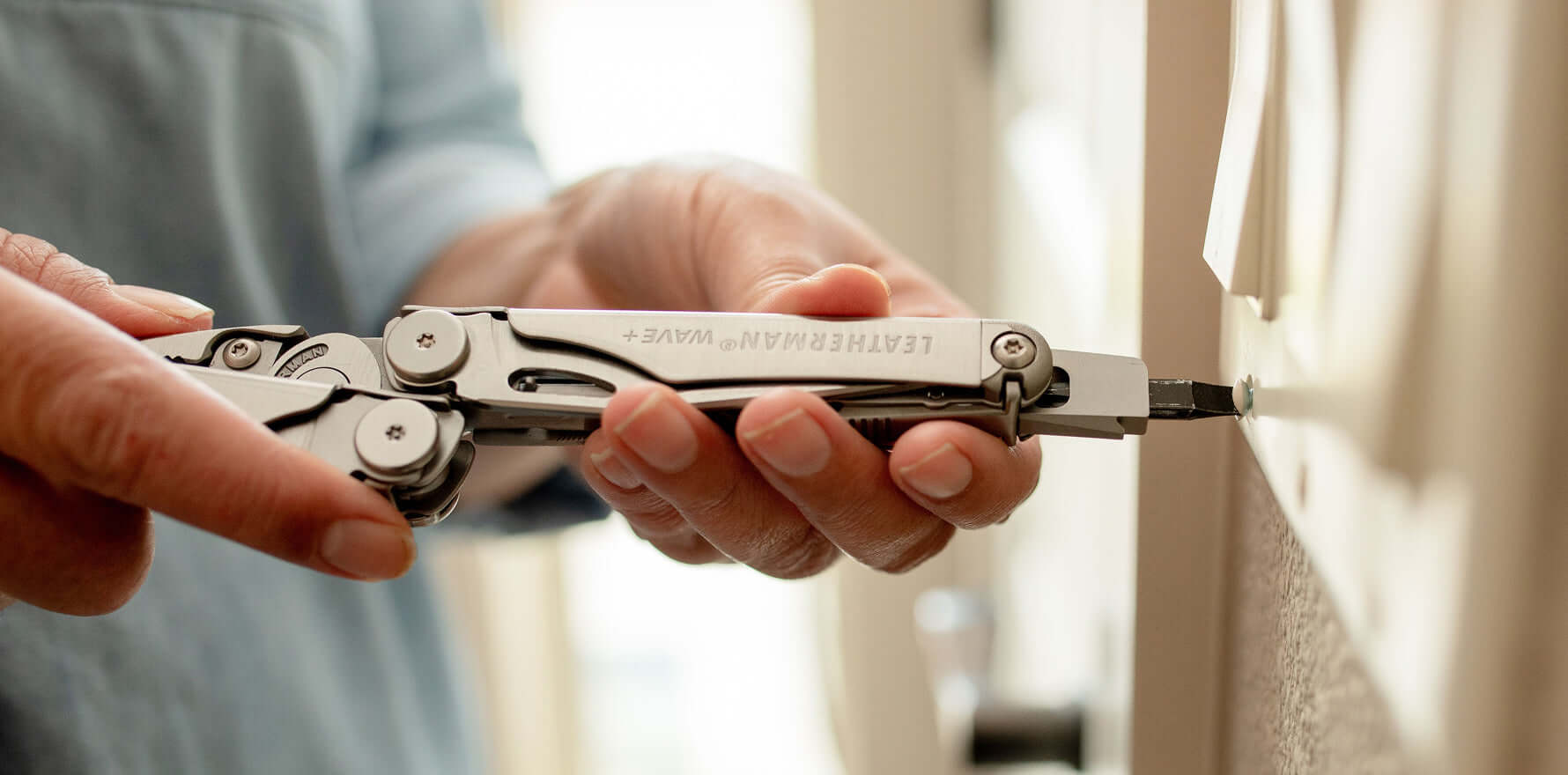 Person using a Leatherman Wave Plus multi-tool to screw on a light switch cover plate.