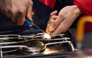 Translation missing: de.A person holds a sparkler to ignite a stove, creating a bright flame in a dimly lit kitchen
