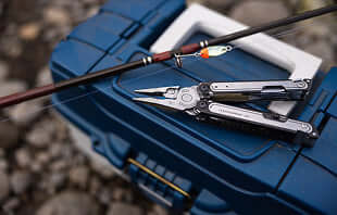 Translation missing: de.A fishing rod, Leatherman Arc, and a fishing pole are resting on the ground, showcasing their equipment for a day of fishing