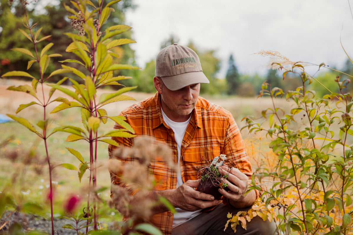 Translation missing: fr.A man in a driftwood colored Leatherman Dad Hat inspecting a newly purchased plant before planting