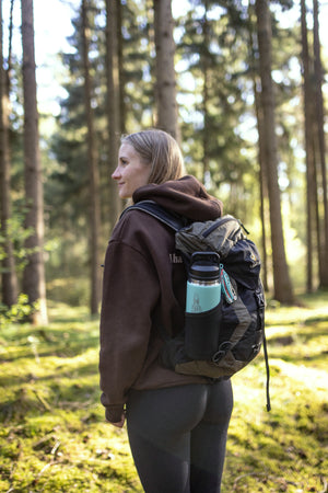 Translation missing: fr.Hiker in a forest carrying a backpack with a mint green Yeti bottle in the side pocket