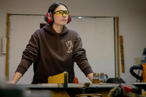 Translation missing: de.A person wearing a brown Leatherman Mr. Wave hoodie standing at a workbench in a workshop, wearing safety glasses and earmuffs