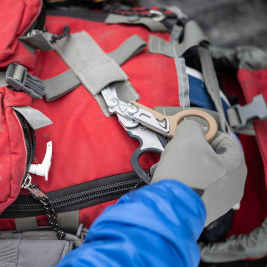 Translation missing: de.Person removing a Coyote/Black Leatherman Raptor® Rescue tool from a red backpack during an outdoor activity