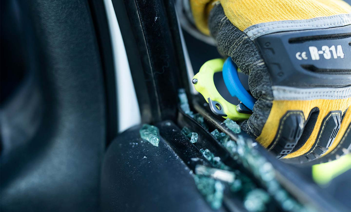 Translation missing: de.Person using yellow and blue Leatherman Raptor® Rescue glass breaker to break a car window