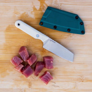 Translation missing: it.A Leatherman Rustle Alpine knife on a wooden cutting board next to a teal sheath and freshly cut chunks of raw fish