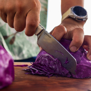 Translation missing: it.A person slicing purple cabbage on a wooden cutting board using a Leatherman Rustle Alpine knife