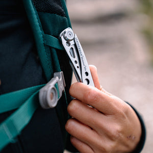 Translation missing: fr.Hand clipping a stainless steel Skeletool KBX pocket knife onto a backpack strap