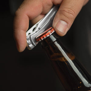 Translation missing: fr.Hand using a stainless steel Skeletool KBX to open a capped glass bottle