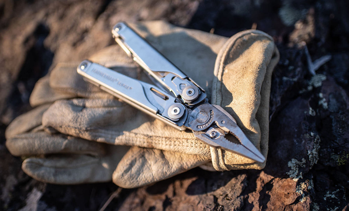 Translation missing: de.Stainless steel Leatherman Surge® multi-tool resting on a leather glove atop a rugged surface
