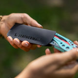 Translation missing: de.A black Leatherman Hypalon tool sleeve held in hand with a partially inserted Paradise-colored Skeletool® CX multi-tool, highlighting the tool’s vibrant design and protective carrying case