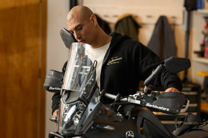 A person wearing a black Leatherman Vintage Zip-Up hoodie standing next to a motorcycle in a garage, with the hoodie’s gold Leatherman logo visible on the chest.