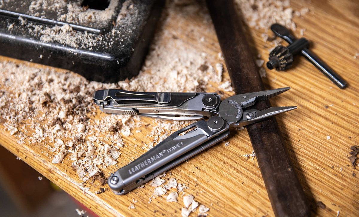 Translation missing: de.Stainless Steel Leatherman Wave® Plus multi-tool on a wood surface with shavings, showcasing its pliers and pocket clip