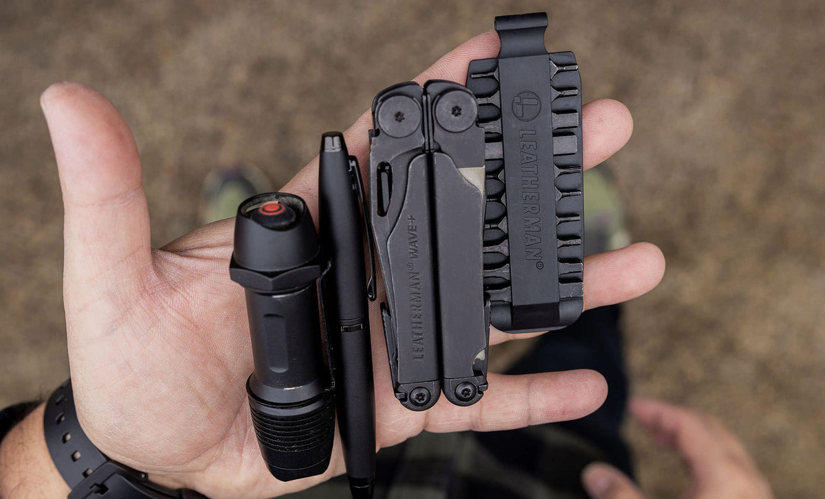 Translation missing: de.Hands showcasing a Black Leatherman Wave® Plus, bit kit, pen, and flashlight